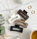 Set of four hair clips in black, white, brown, and beige on a marble surface with decorative items.