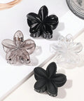 Set of four flower-shaped hair clips in black, clear, and transparent on a white background.