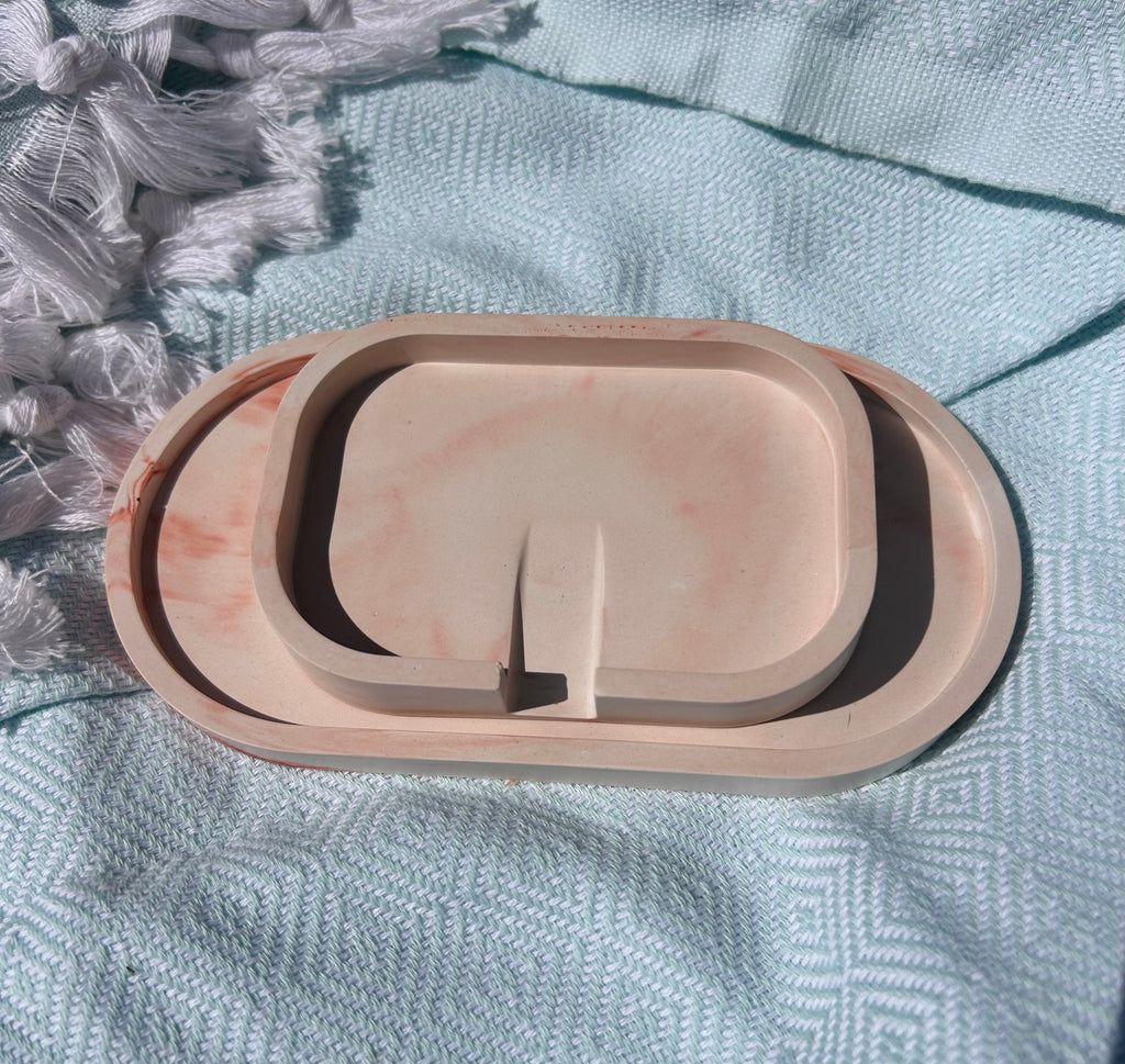 A three-tier oval ceramic tray set in a light peach-beige color with subtle pinkish-orange marbling, displayed on a textured light blue woven blanket.