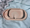 A three-tier oval ceramic tray set in a light peach-beige color with subtle pinkish-orange marbling, displayed on a textured light blue woven blanket.