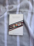 A Muga Muga Jewellery bracelet with a colorful, iridescent round cabochon and gold-toned metal accents, wrapped in black, red, and white cords. The card is displayed on a gray and white striped textured fabric background.