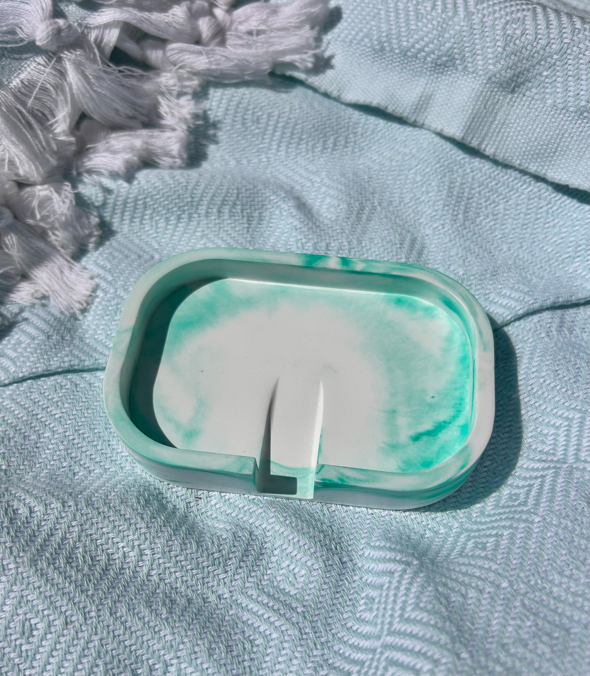 A translucent green and white resin soap dish with a small integrated stand, resting on a textured light blue blanket.