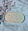 An oval handmade soap bar with a half-and-half design, resting on a textured light blue fabric next to white tassels.