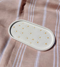 An oval cream-colored silicone tray with a daisy pattern, placed on a pink and white striped fabric background.