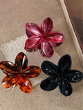 Three flower-shaped hair clips in red, orange, and black on a textured surface.