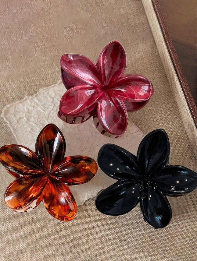 Three flower-shaped hair clips in red, orange, and black on a textured surface.